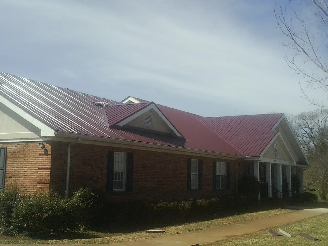 Red metal roof with gabled entries on a long brick building, from a Hail Damage Roof Repair job in Lisle